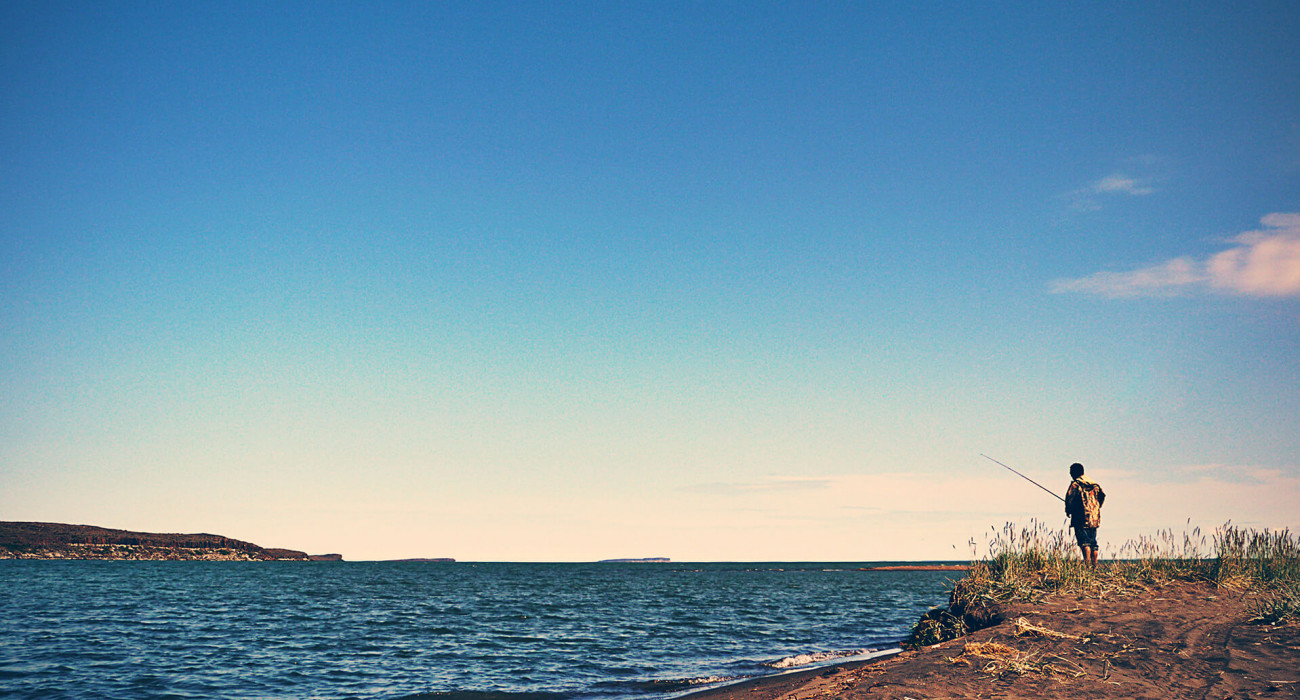 Person standing on the shore, fishing with rod